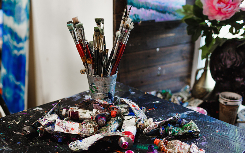 table covered with paint brushes and tubes of oil paints