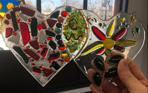 hand holding two fused glass hearts
