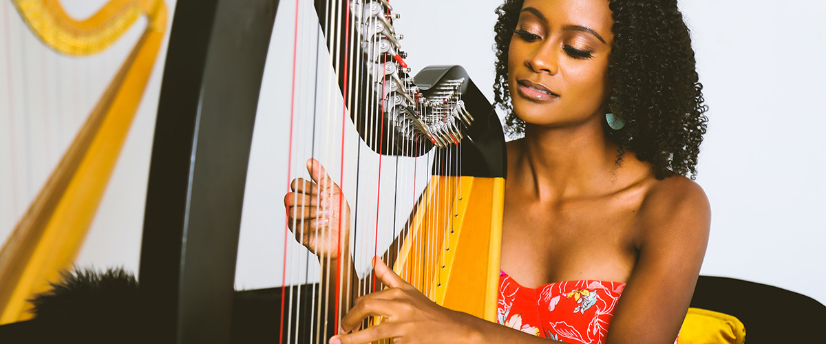 Angelica Hairston, harpist, posing with her fingers on the strings of her harp