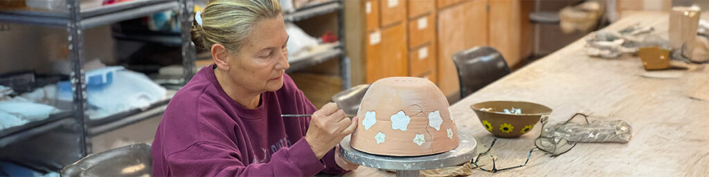 An adult women painting her pottery in our workshop