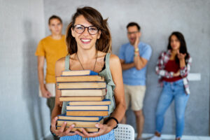 Young adults with one holding a stack of books.